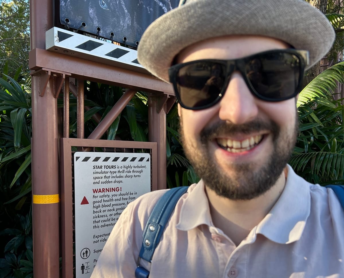Juan in front of a warning sign outside the Star Tours Disney ride. The sign reads: Star Tours is a highly turbulent simulator-type thrill ride through space.